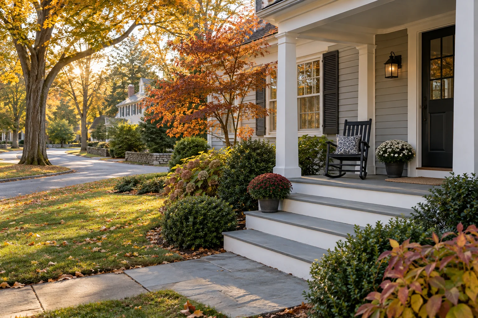 A well-kept New England colonial porch in autumn with clean steps and a simple chair.